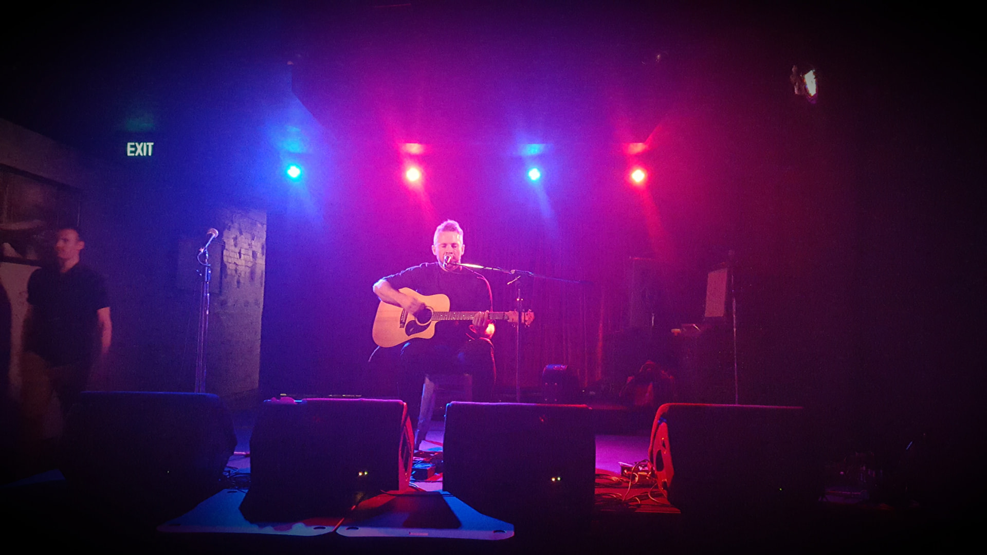 Dan Smith performing solo with acoustic guitar under blue and red stage lights at a Brisbane live music venue