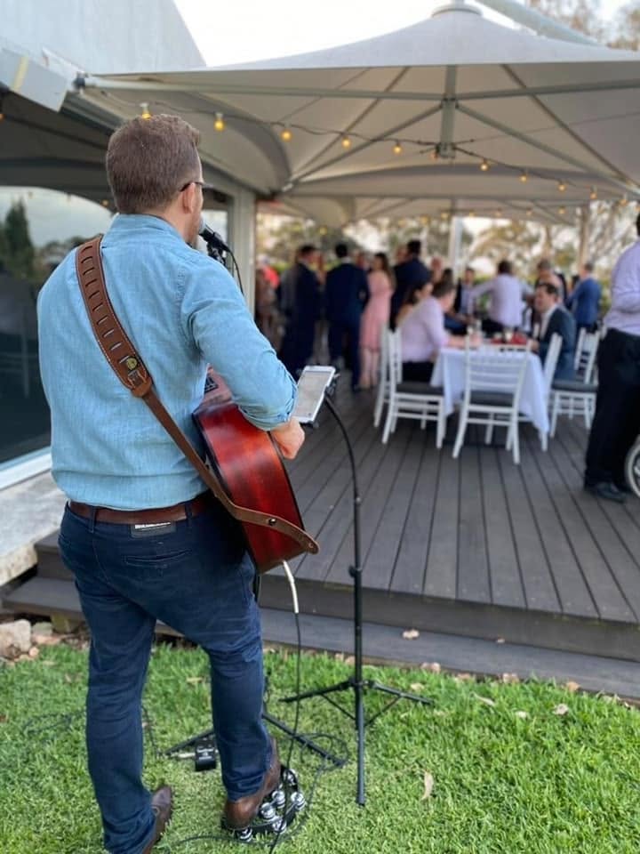 Dan Smith performing acoustic guitar at an outdoor wedding reception under a marquee