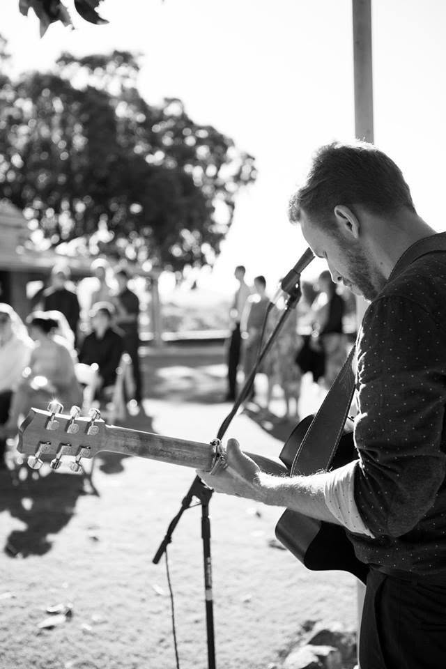 Black and white close-up of Dan Smith playing acoustic guitar at an outdoor wedding ceremony