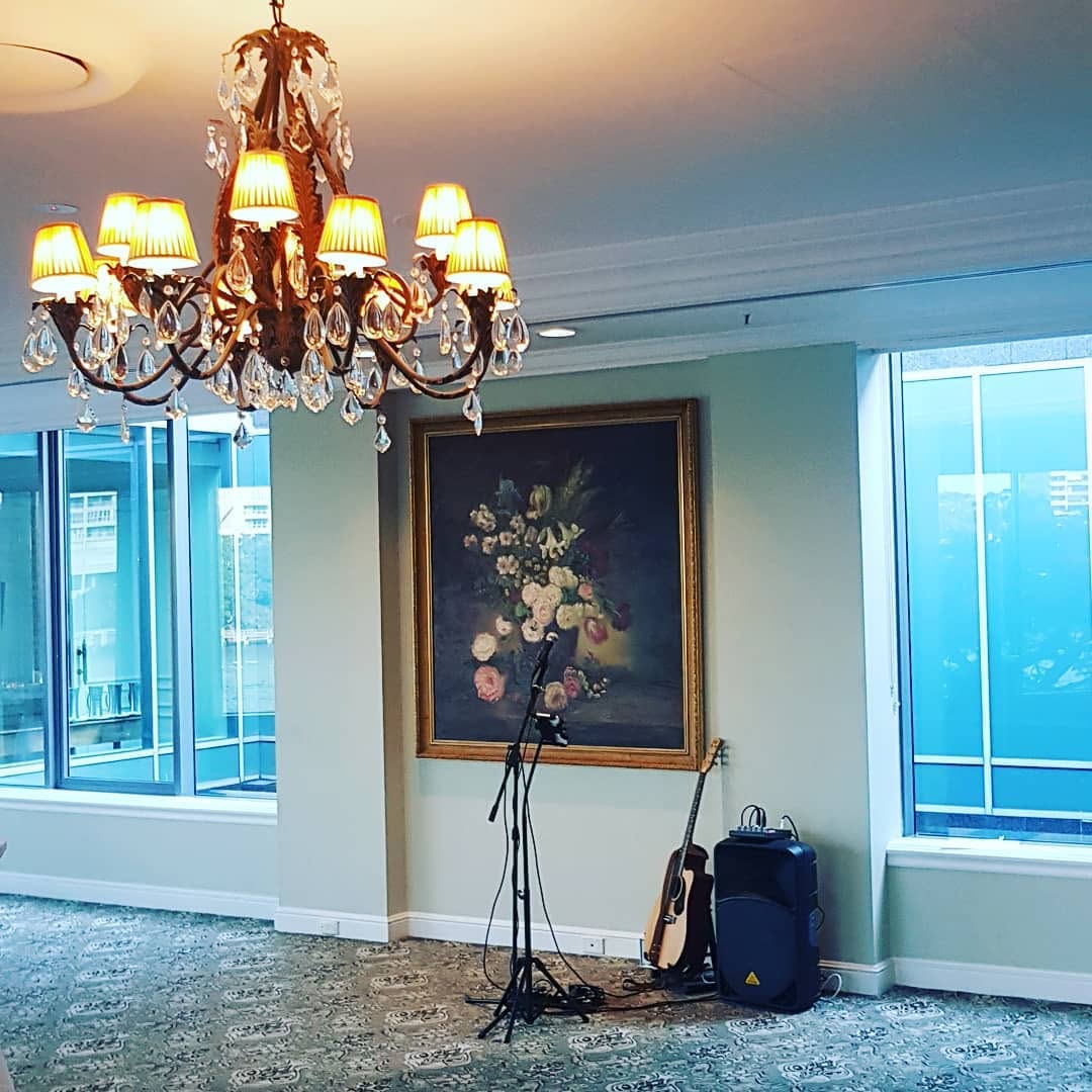 Guitar, microphone stand and speaker set up beneath a crystal chandelier in an elegant function room